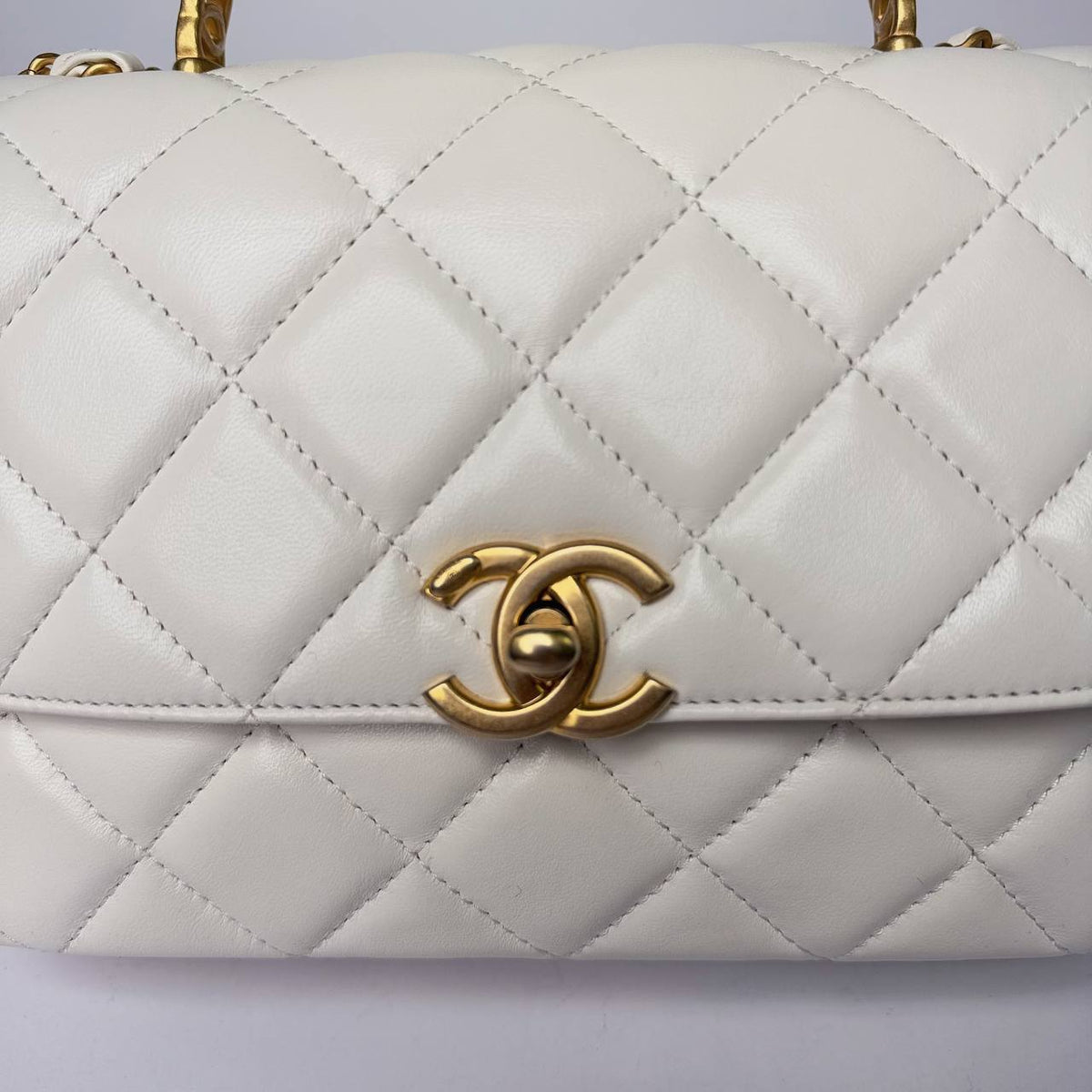 Chanel Small Top Handle Flap Bag white, close-up of the gold CC turnlock on quilted lambskin