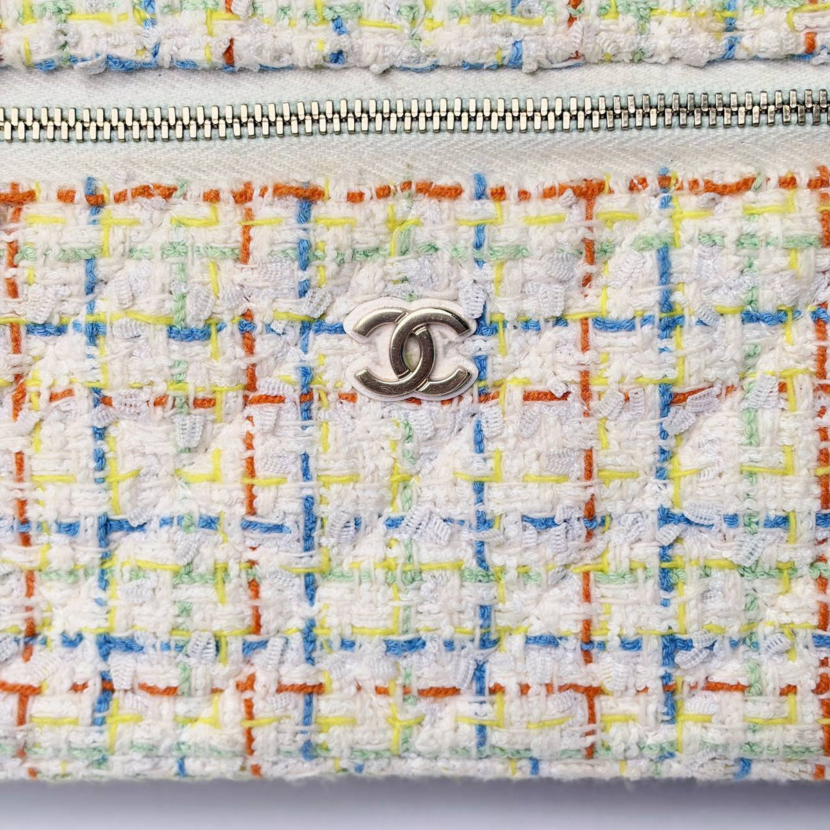 Chanel Slim Vanity Case white tweed, close-up of the silver CC logo and zipper on blue, orange and yellow check